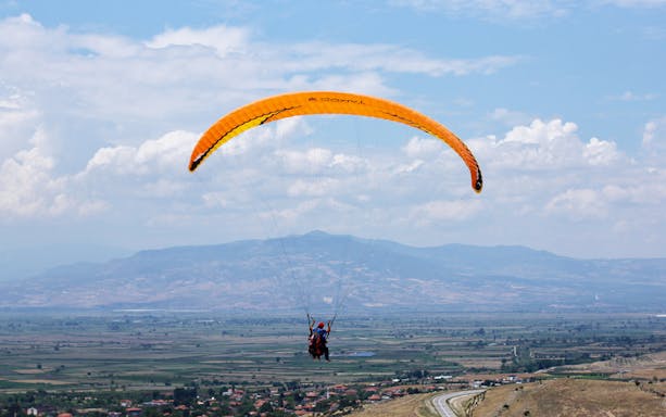 Tandem paragliding over Pamukkale landscape with mountains in the background.