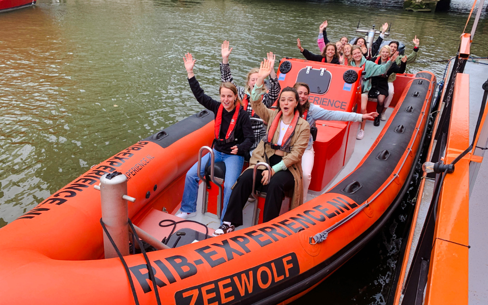 Group enjoying Rotterdam Harbour tour on RIB speedboat, waving and smiling.