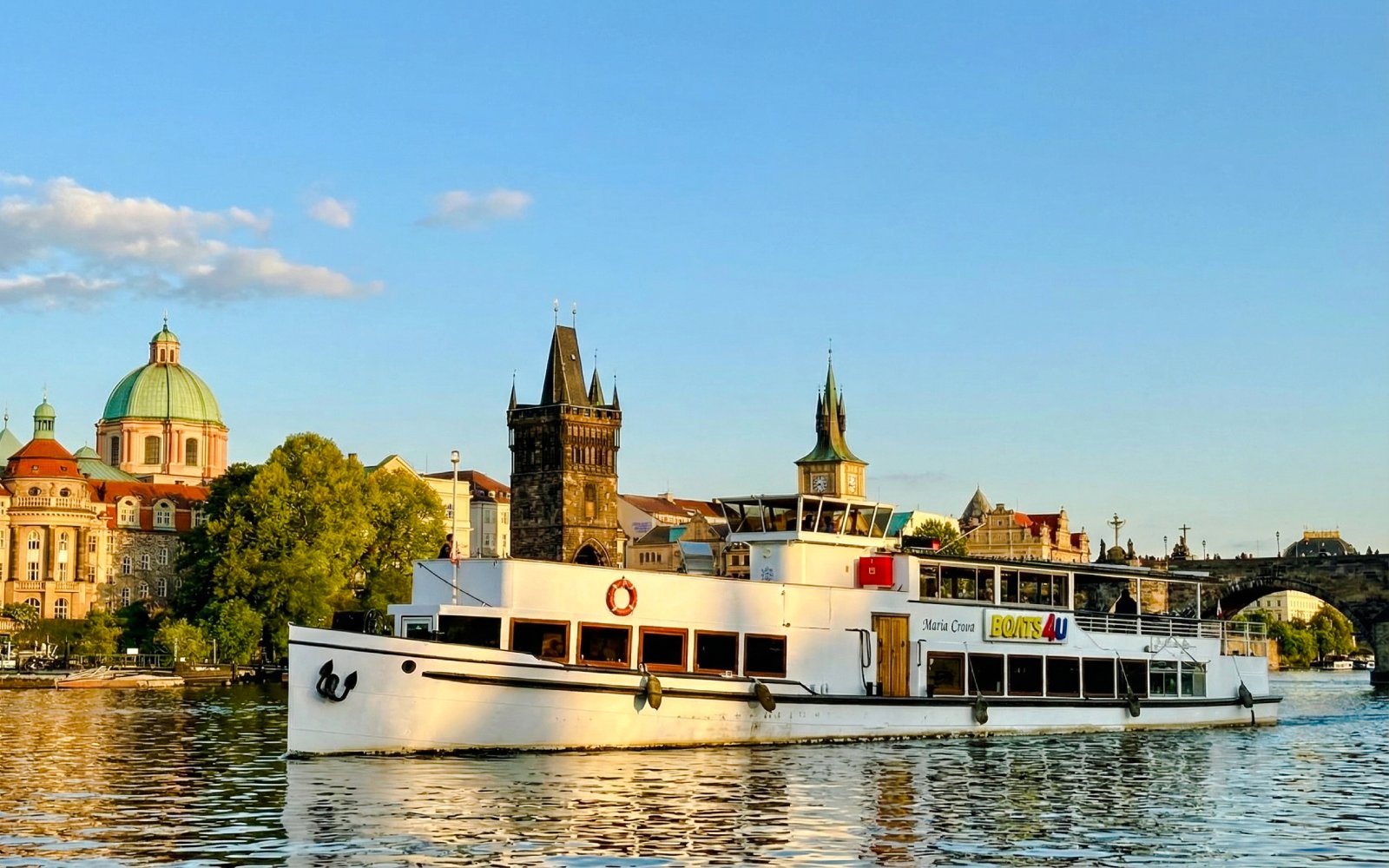Cruise boat on Vltava River with Prague's historic buildings in the background.