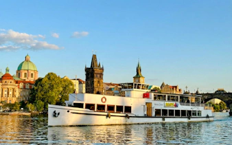 Cruise boat on Vltava River with Prague's historic buildings in the background.