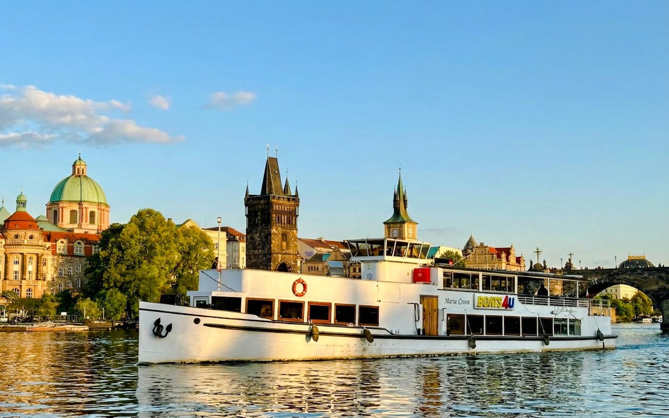 Cruise boat on Vltava River with Prague's historic buildings in the background.