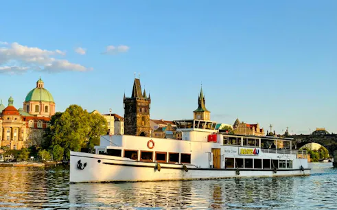 Cruise boat on Vltava River with Prague's historic buildings in the background.