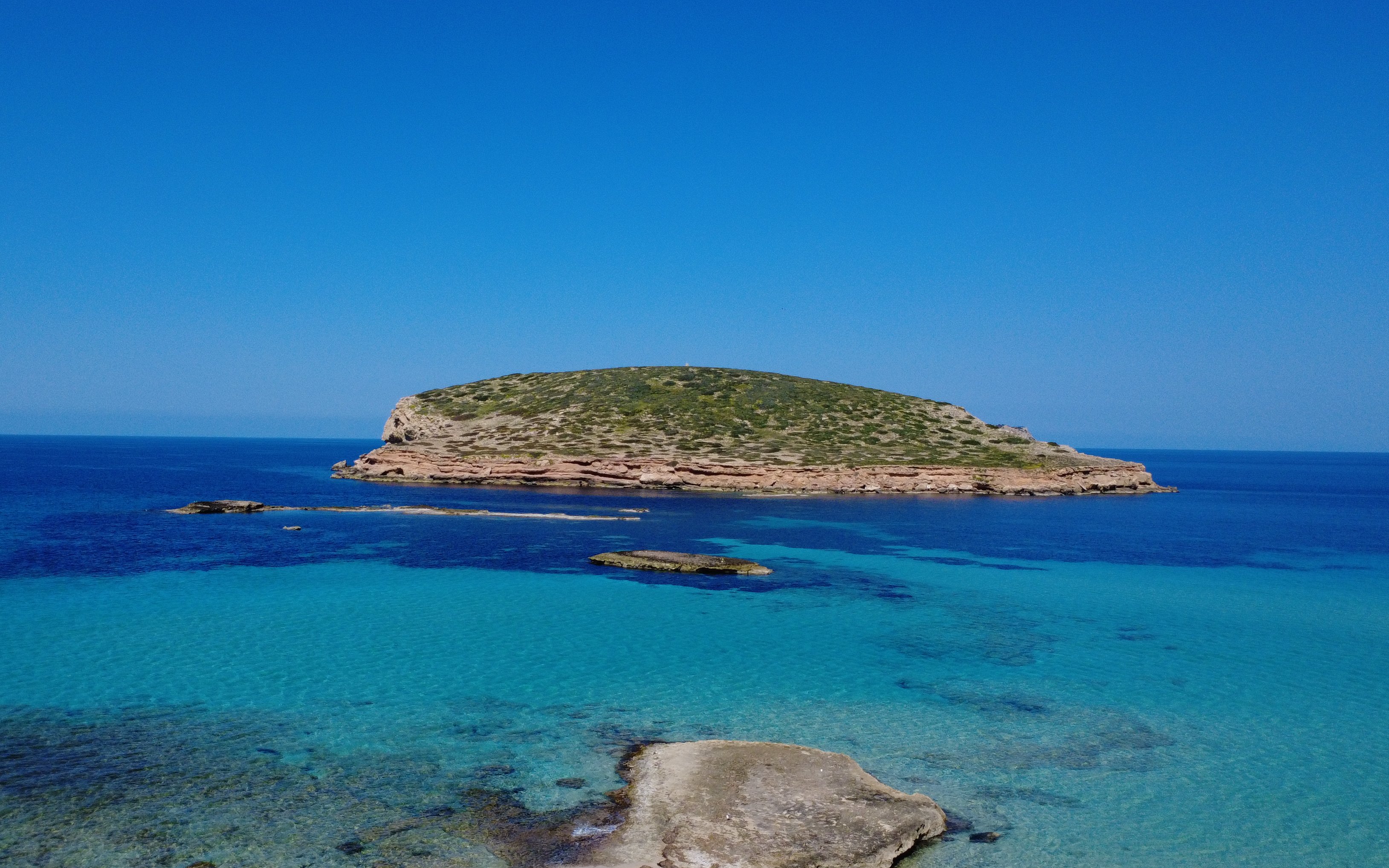 Cala Comte beach with clear turquoise waters and rocky islet in Ibiza, Spain.