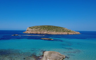 Cala Comte beach with clear turquoise waters and rocky islet in Ibiza, Spain.