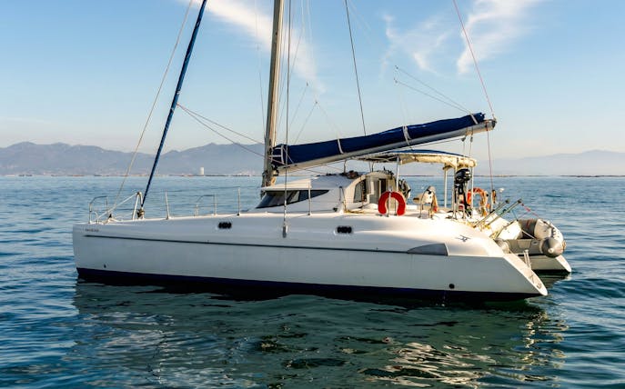 Catamaran sailing in La Maddalena Archipelago with distant mountains.