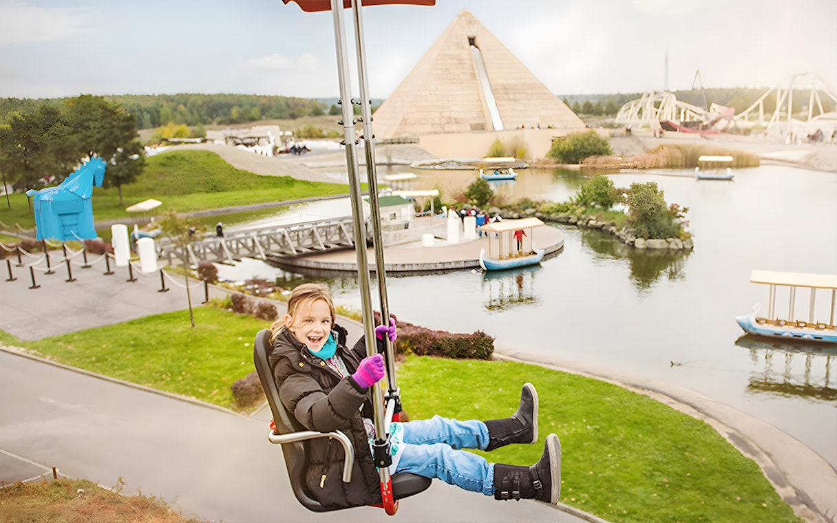 Child enjoying a ride at Belantis Adventure Park with pyramid and lake in background.