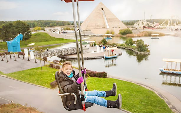 Child enjoying a ride at Belantis Adventure Park with pyramid and lake in background.