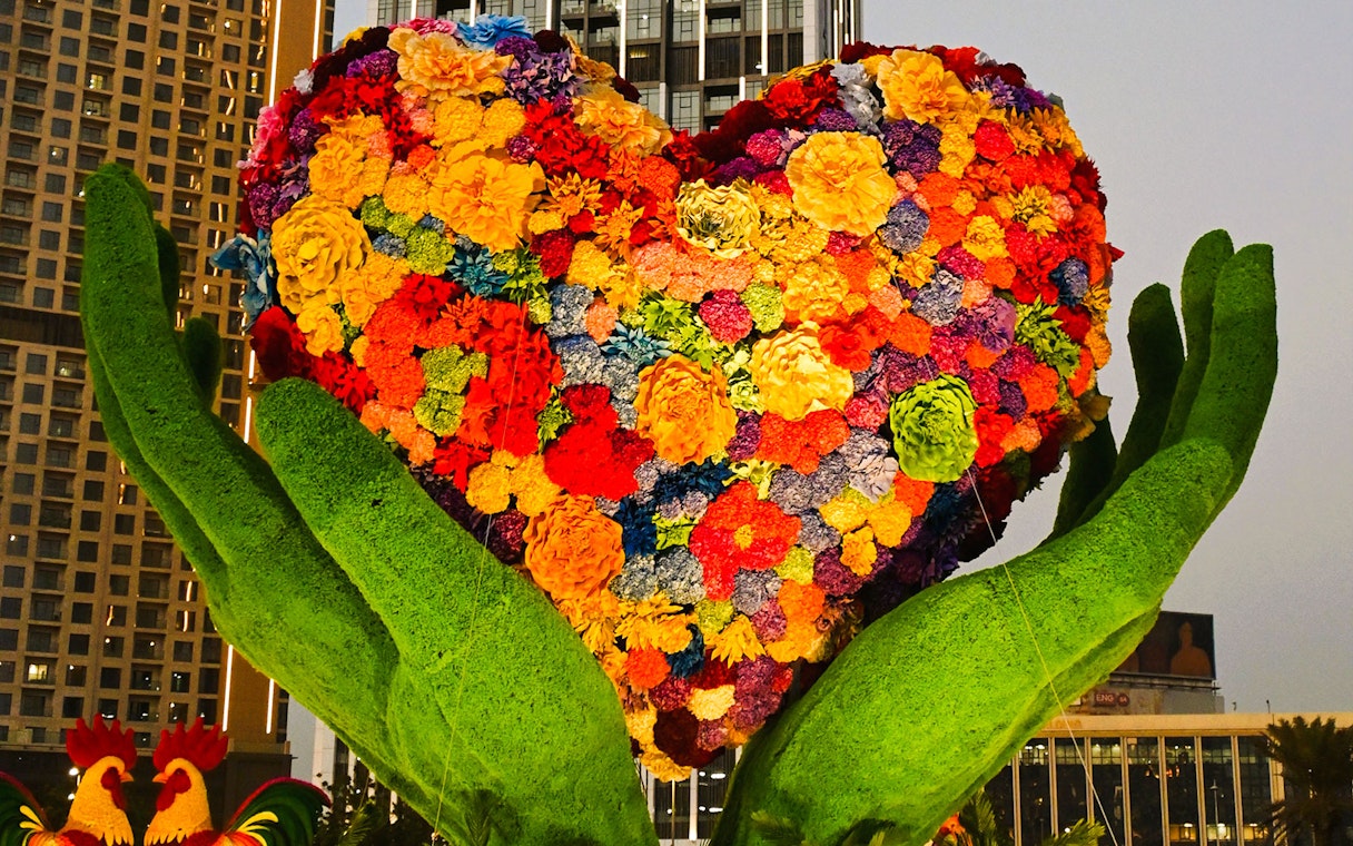 Floral heart sculpture held by green hands at Dubai Garden Glow.