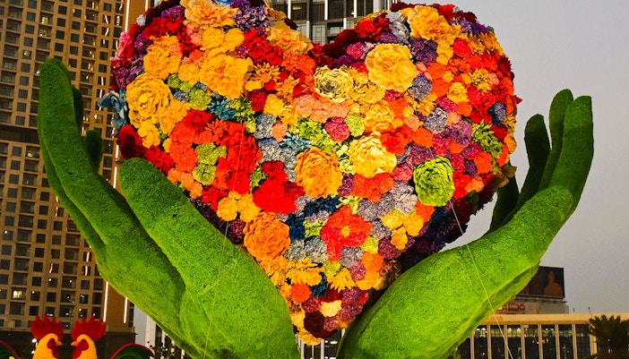 Floral heart sculpture held by green hands at Dubai Garden Glow.