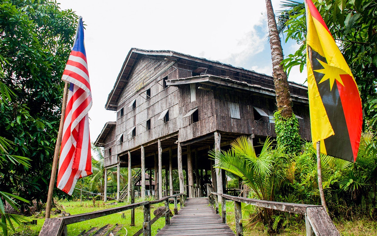 Traditional longhouse at Sarawak Cultural Village, Malaysia, with flags and lush greenery.