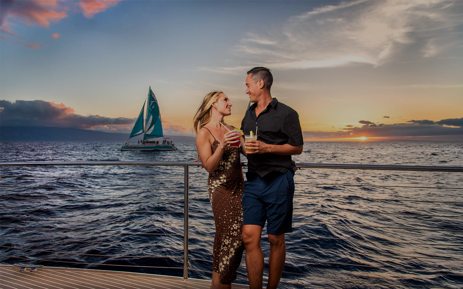 Couple enjoying drinks on a luxury sailboat at sunset in Maui, Hawaii.