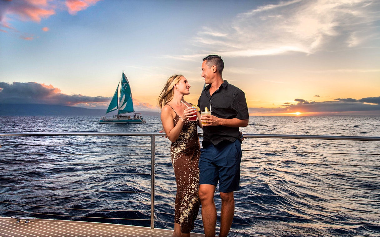 Couple enjoying drinks on a luxury sailboat at sunset in Maui, Hawaii.