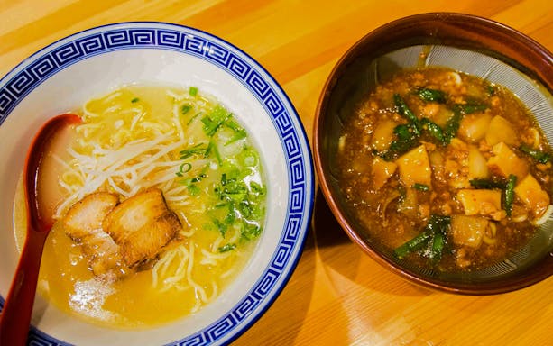 Bowl of ramen with pork and scallions next to a bowl of spicy tofu soup in a Ramen Kitchen Experience.