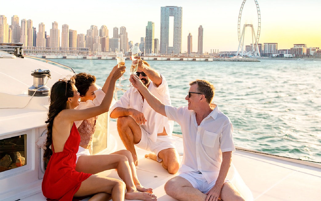 Group enjoying a toast on a yacht with Dubai skyline and Ferris wheel in the background.