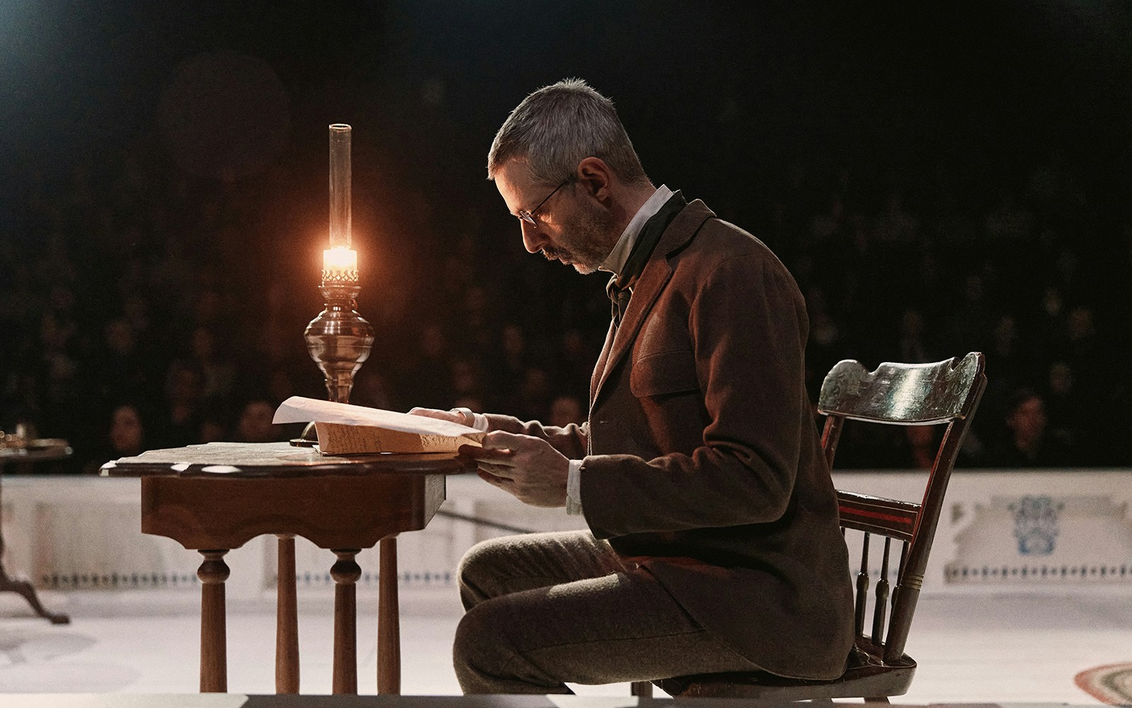 Man reading at a desk by lamplight during "An Enemy of the People" performance.
