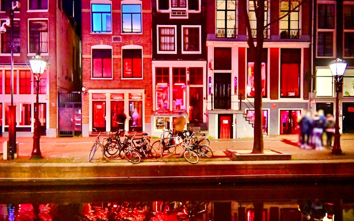 Bicycles parked along canal in Amsterdam Red Light District at night.