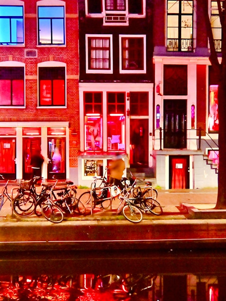 Bicycles parked along canal in Amsterdam Red Light District at night.