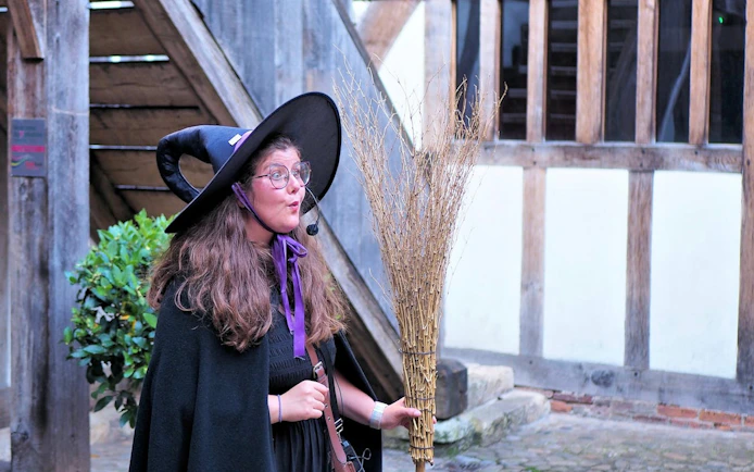 Tour guide in witch costume holding broom on York Witches & History Old Town Walking Tour.
