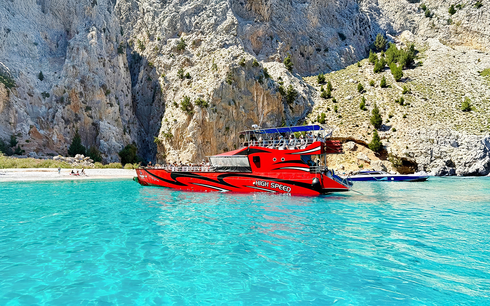 High-speed cruise boat on turquoise waters near rocky cliffs, Rhodes.