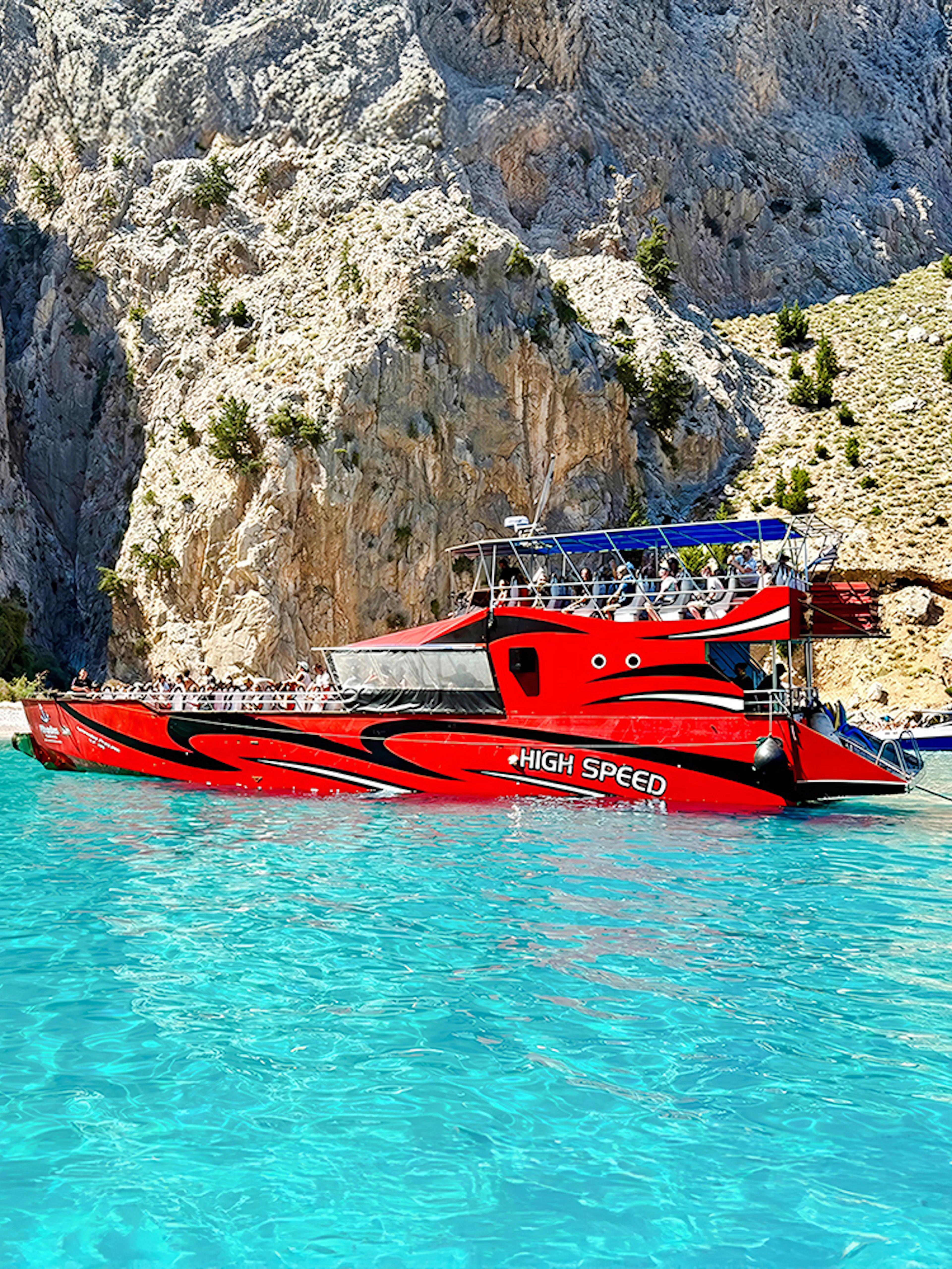 High-speed cruise boat on turquoise waters near rocky cliffs, Rhodes.