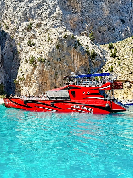 High-speed cruise boat on turquoise waters near rocky cliffs, Rhodes.