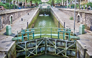 Canal lock on Canal Saint-Martin in Paris, France, with surrounding walkways and greenery.