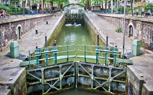 Canal lock on Canal Saint-Martin in Paris, France, with surrounding walkways and greenery.