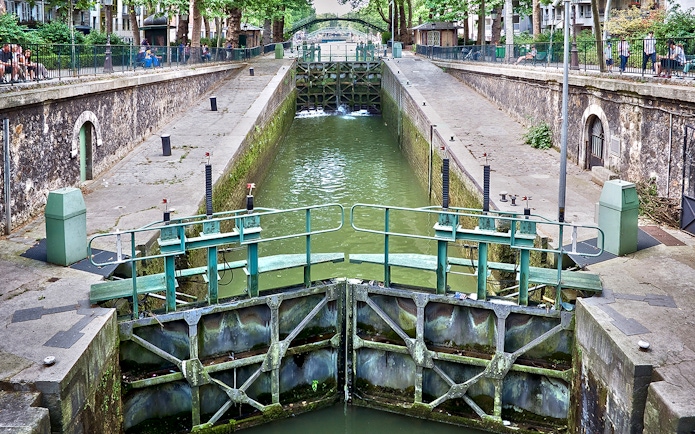 Canal lock on Canal Saint-Martin in Paris, France, with surrounding walkways and greenery.