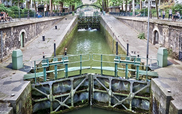 Canal lock on Canal Saint-Martin in Paris, France, with surrounding walkways and greenery.