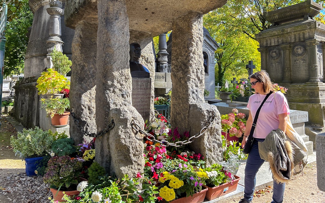 Visitor at Père Lachaise cemetery admiring a flower-adorned tombstone.