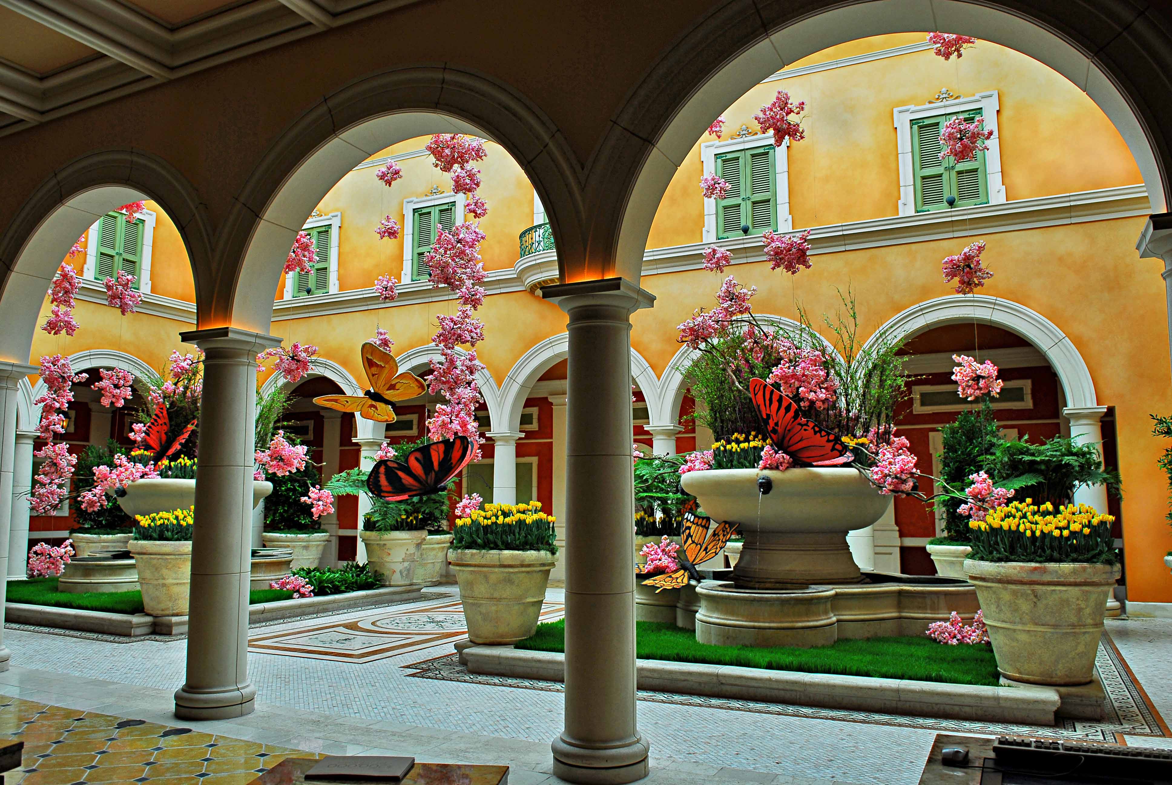 Courtyard with arches, pink flowers, large butterfly sculptures, and potted plants.