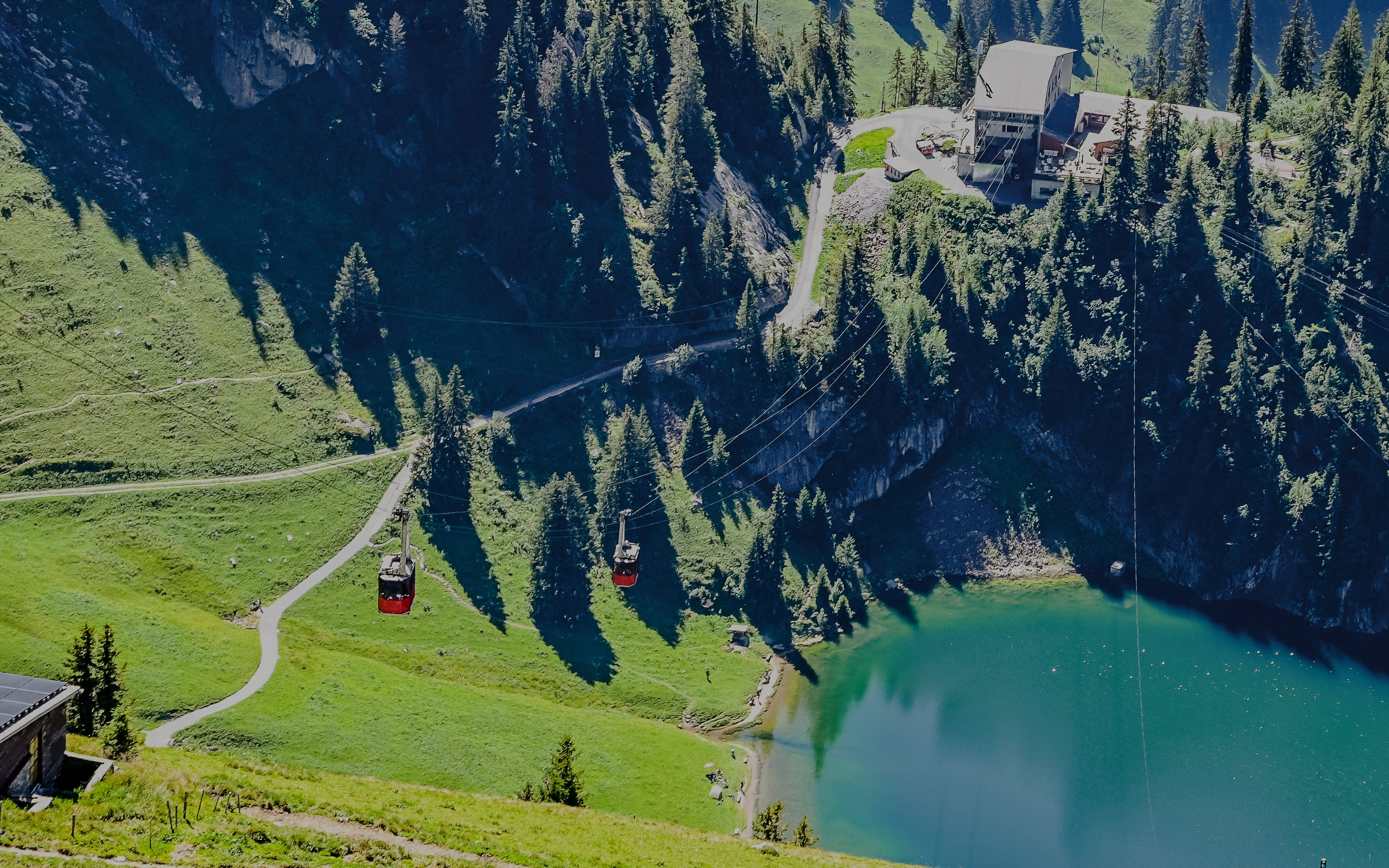 Cable cars traveling over Stockensee Lake surrounded by lush green hills and forest.