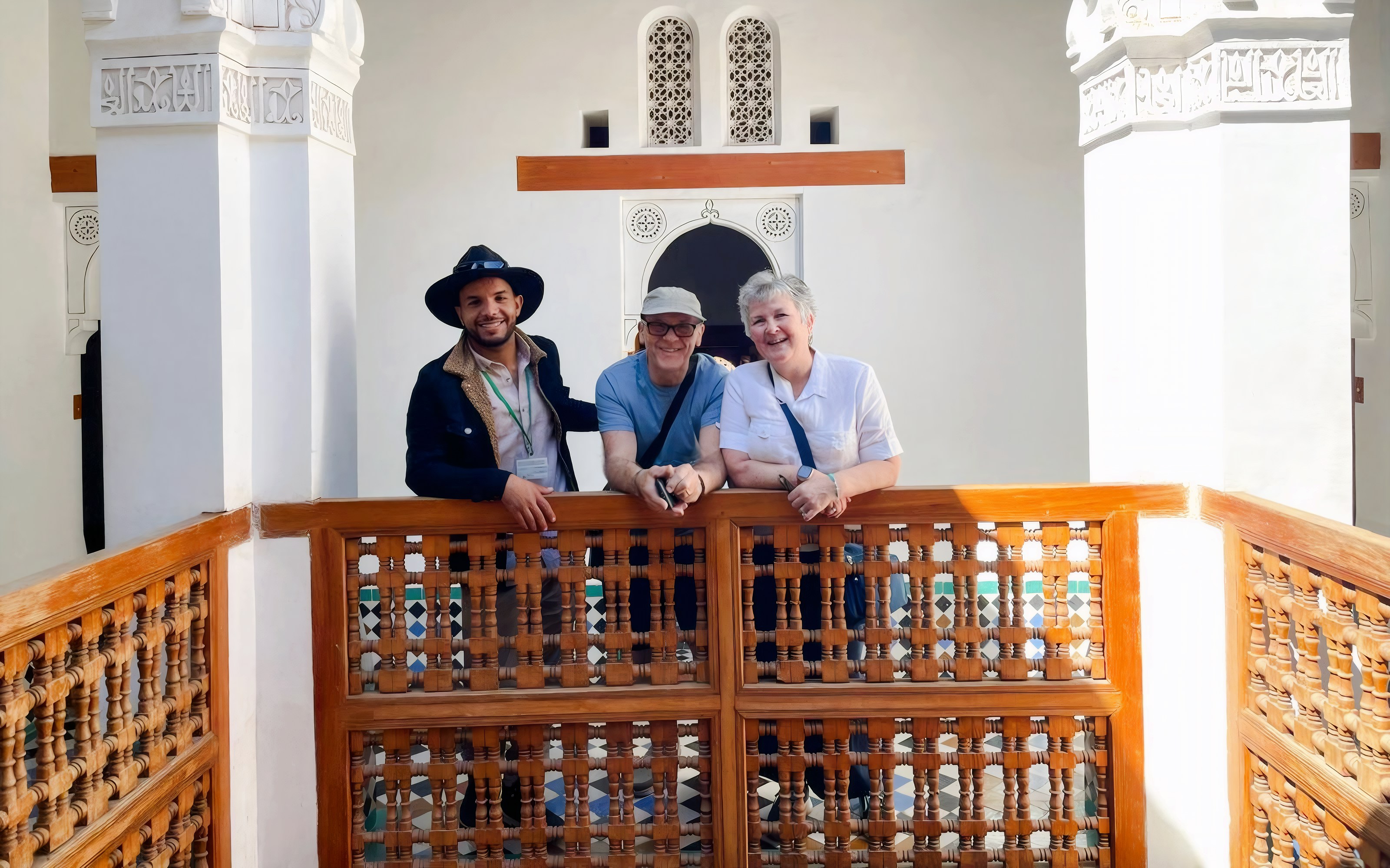 Guide with tourists at Bahia Palace, Marrakech, standing by intricate wooden railing.