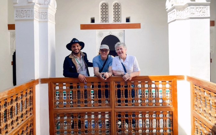 Guide with tourists at Bahia Palace, Marrakech, standing by intricate wooden railing.