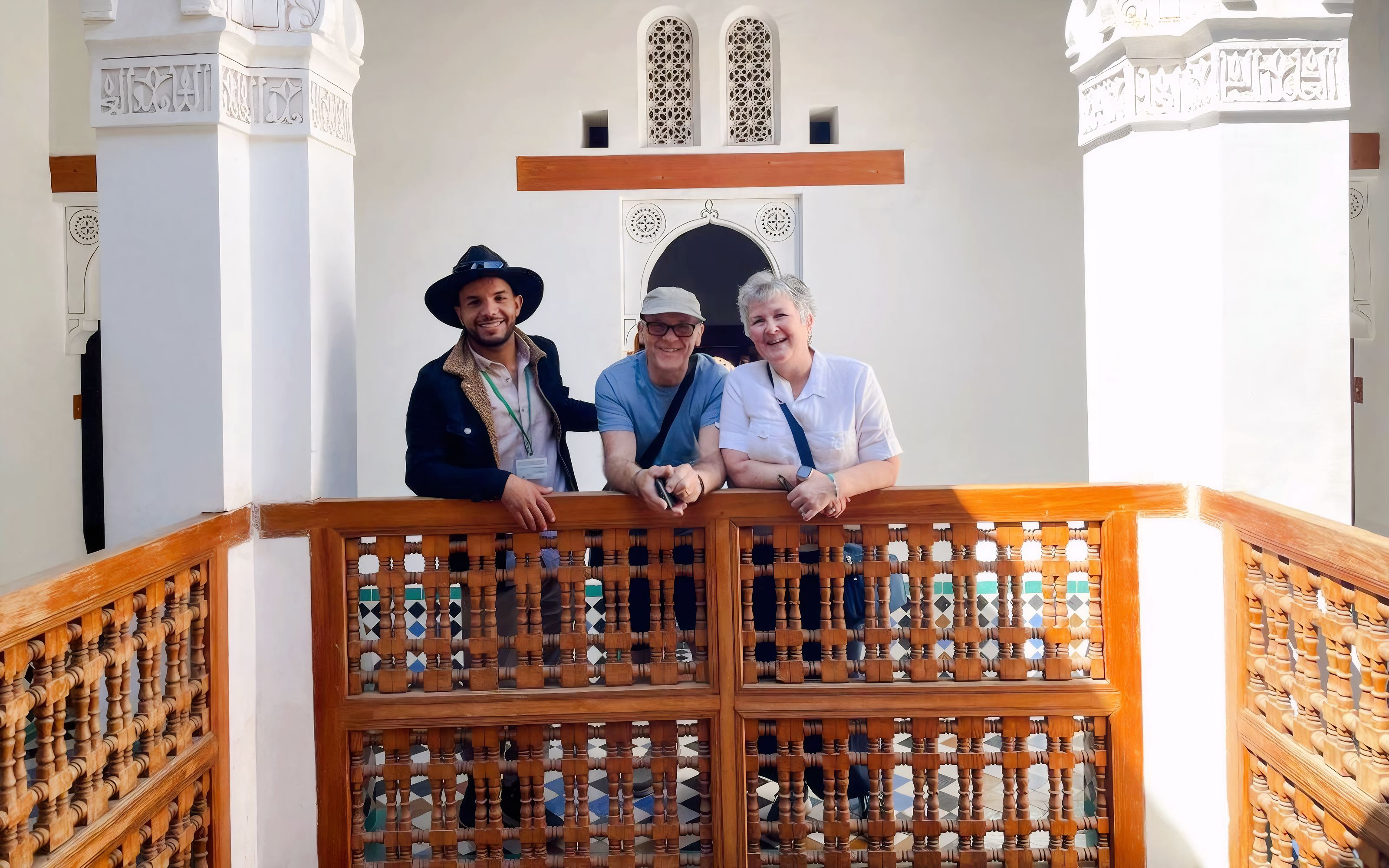 Guide with tourists at Bahia Palace, Marrakech, standing by intricate wooden railing.