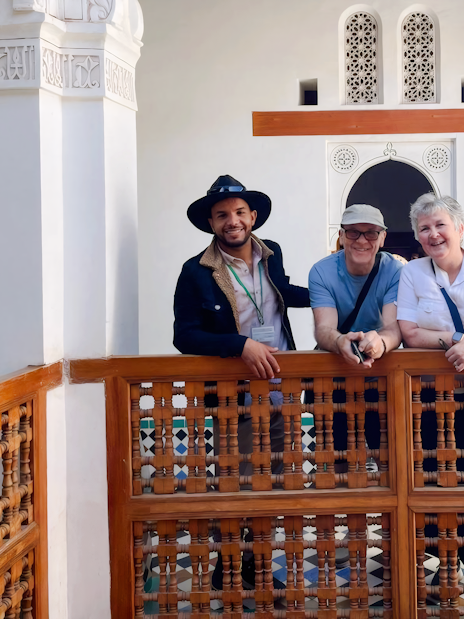 Guide with tourists at Bahia Palace, Marrakech, standing by intricate wooden railing.