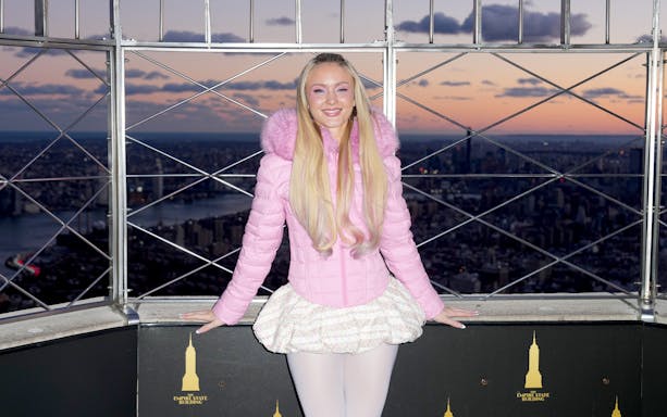 Person in pink jacket at Empire State Building observatory, New York City skyline at sunset.