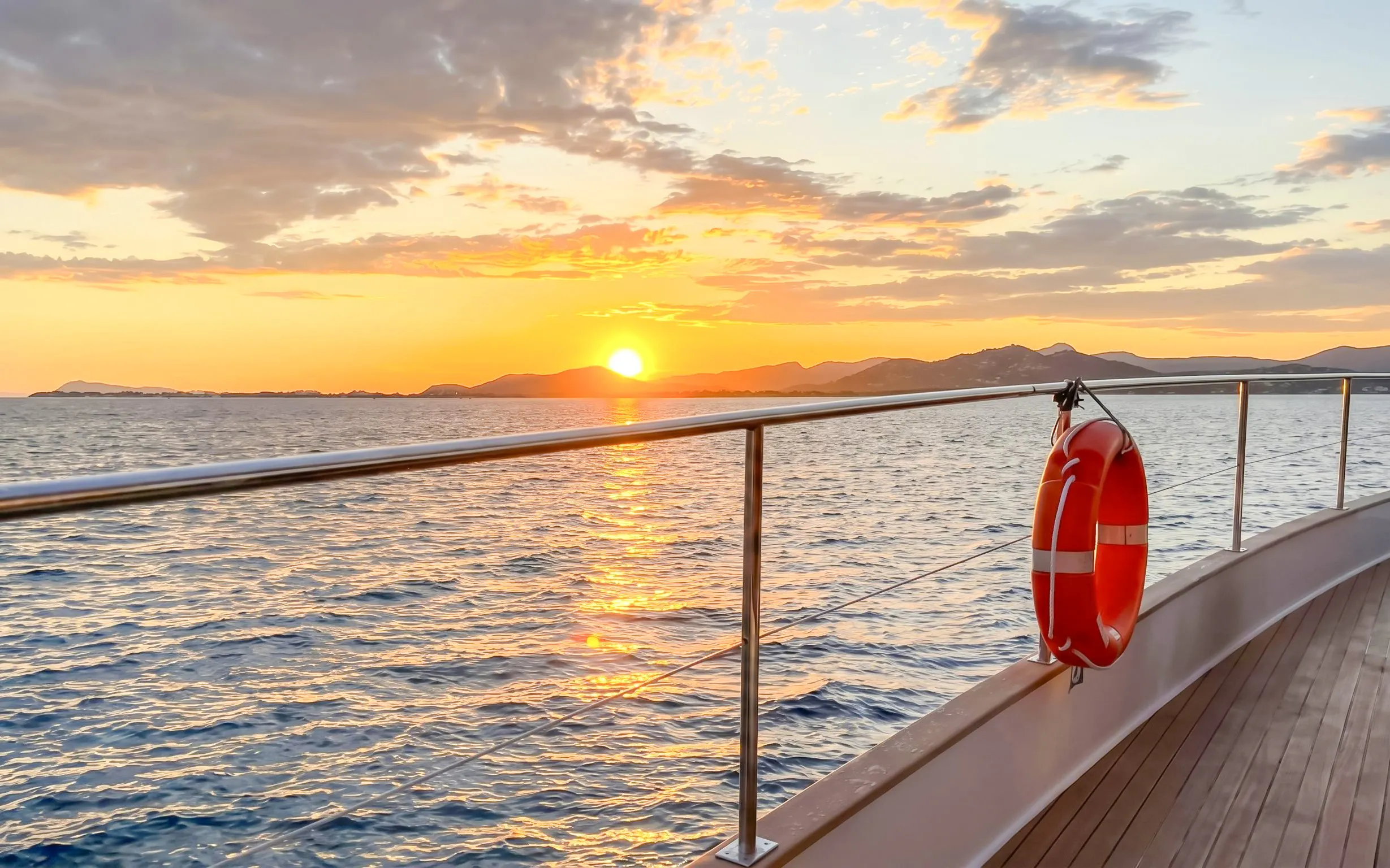 Catamaran deck at sunset with ocean view and distant hills.