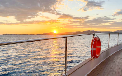 Catamaran deck at sunset with ocean view and distant hills.