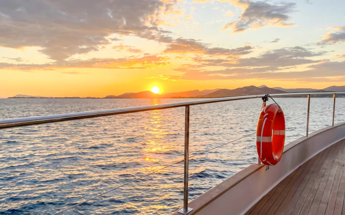 Catamaran deck at sunset with ocean view and distant hills.