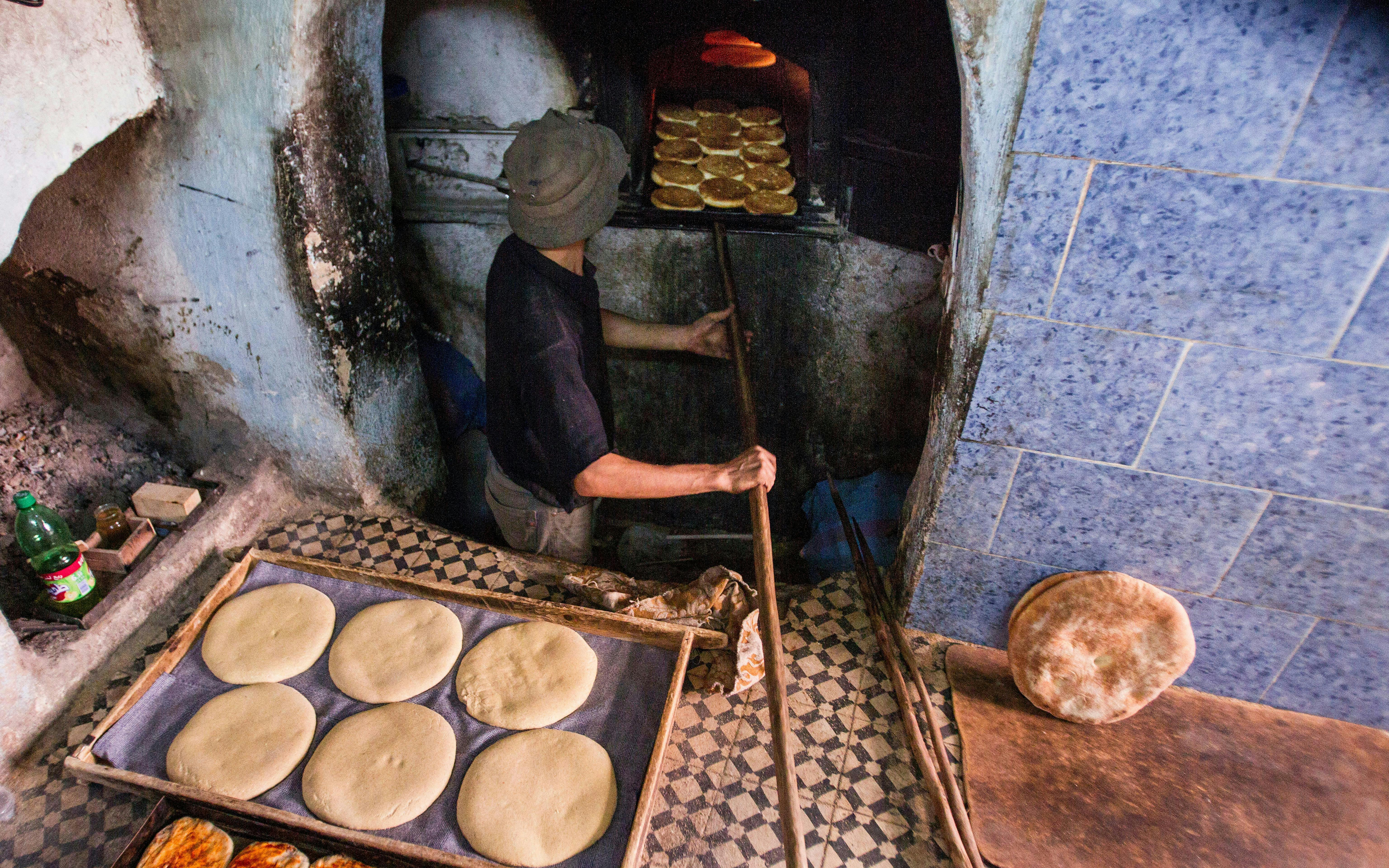 Baker placing bread in a traditional oven in Fes, Morocco.