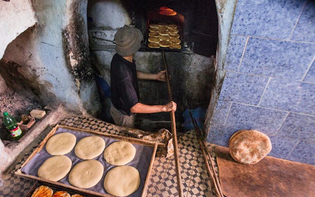 Baker placing bread in a traditional oven in Fes, Morocco.