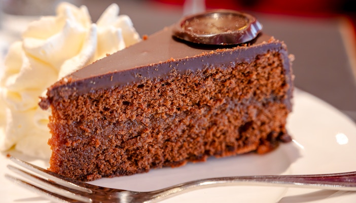 Sachertorte chocolate cake slice with whipped cream on a plate.