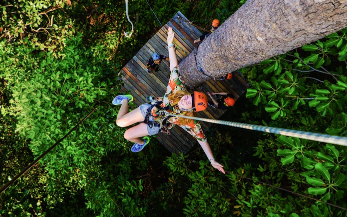 Tourist zip lining through lush forest at Hanuman World Zipline, Thailand.
