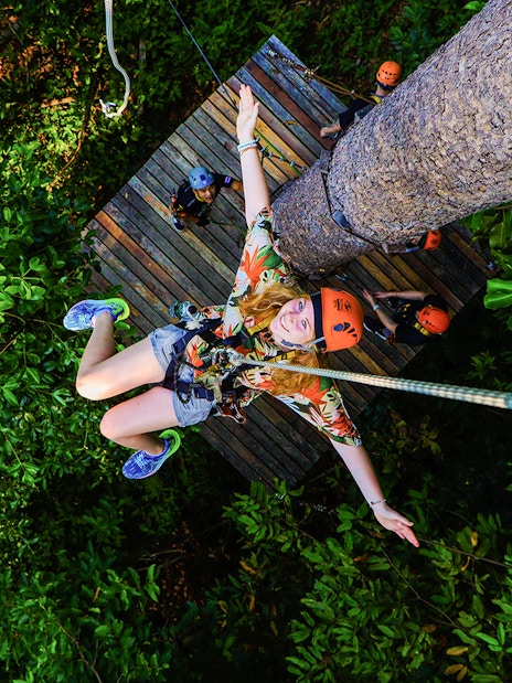 Tourist zip lining through lush forest at Hanuman World Zipline, Thailand.