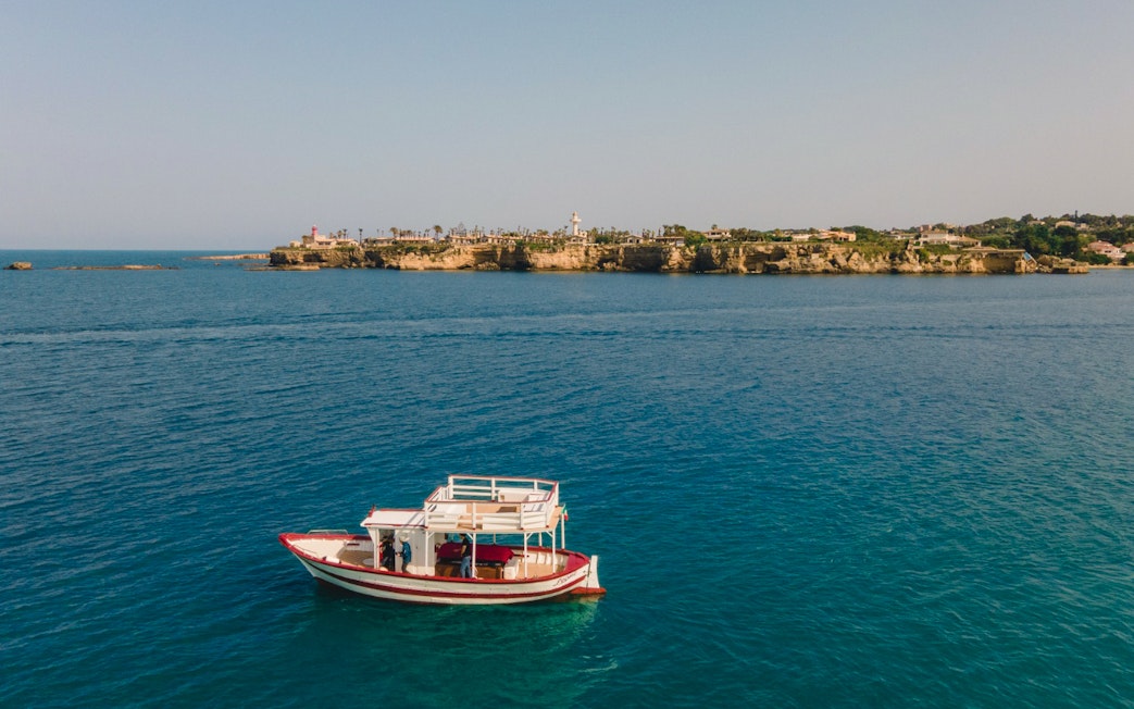 Boat near Ortigia Island with sea caves in the background, Sicily tour.