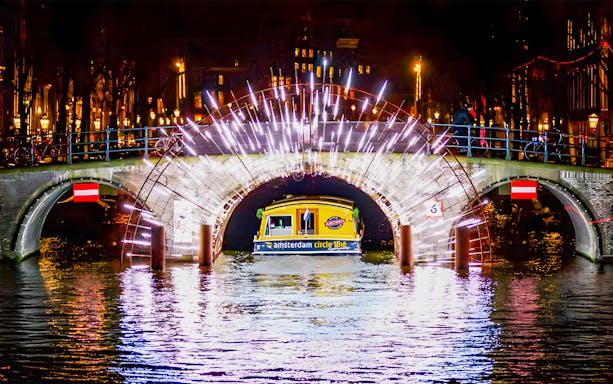 Amsterdam canal bridge illuminated during Light Festival cruise.