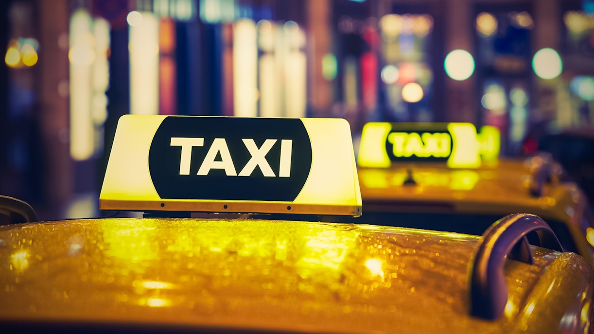 Taxi sign illuminated at night in a city setting.