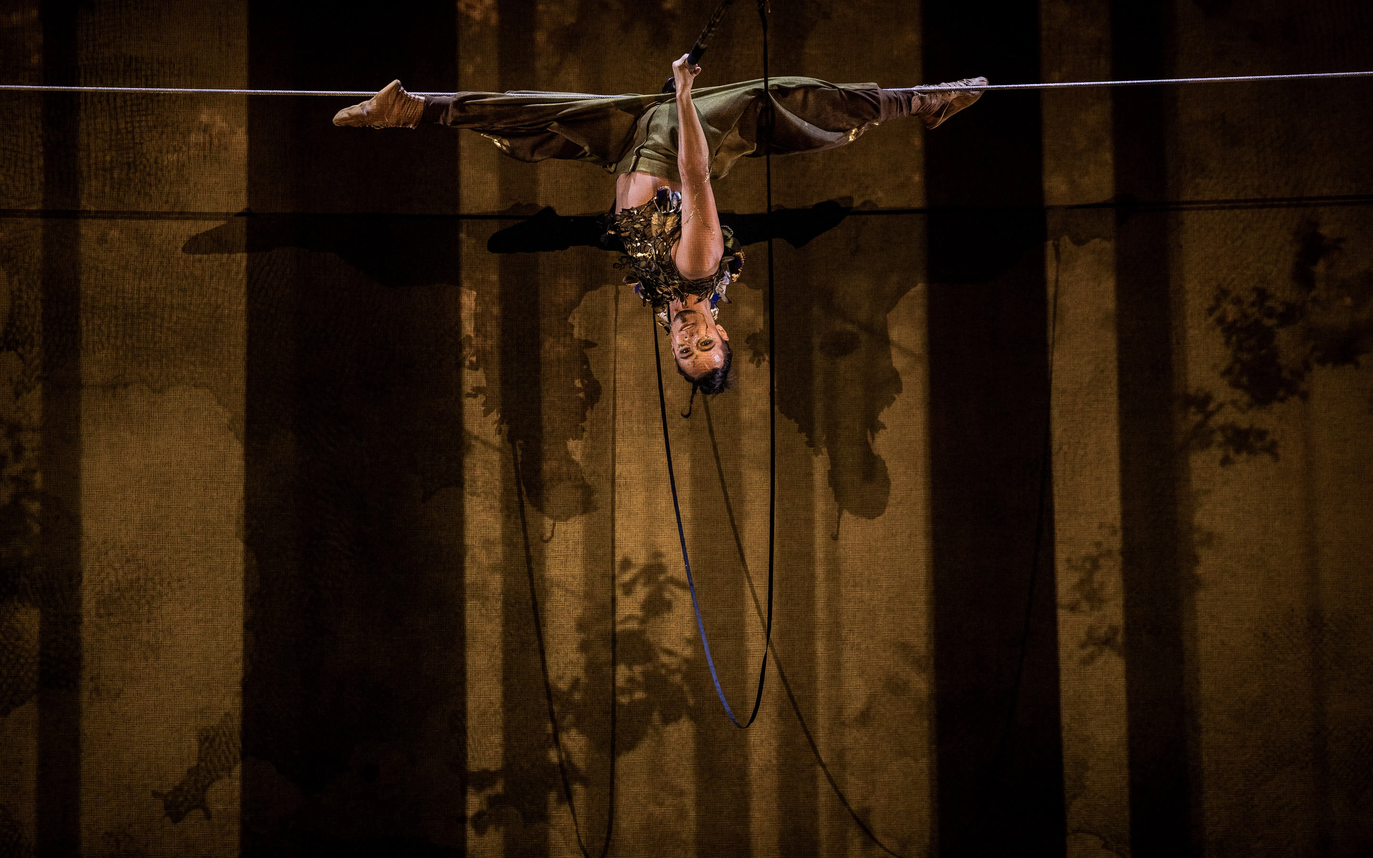 Performer suspended upside down during Cirque du Soleil Alizé stage show.