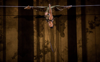 Performer suspended upside down during Cirque du Soleil Alizé stage show.